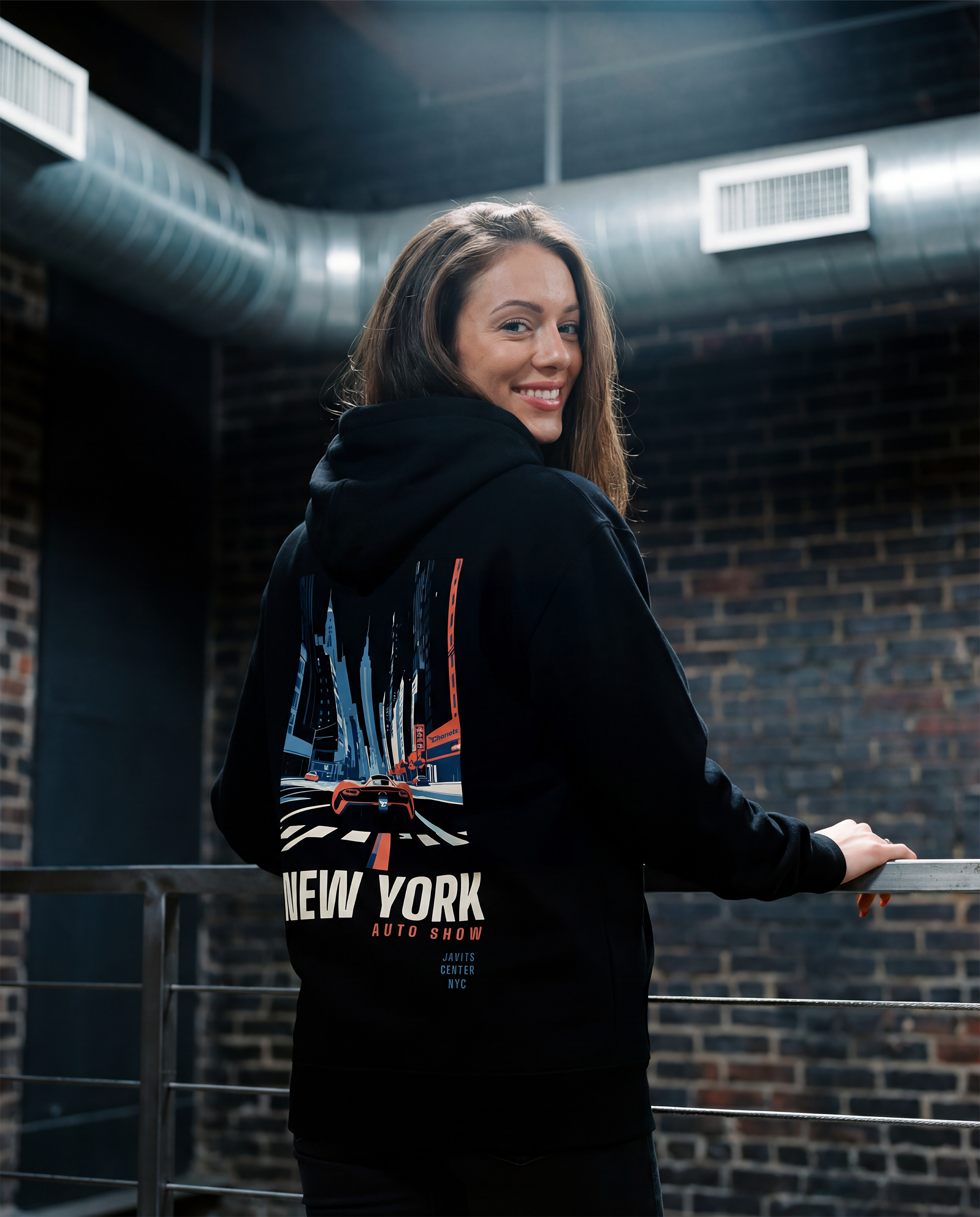 Woman wearing a black hoodie with 'New York' text, standing in an industrial setting.