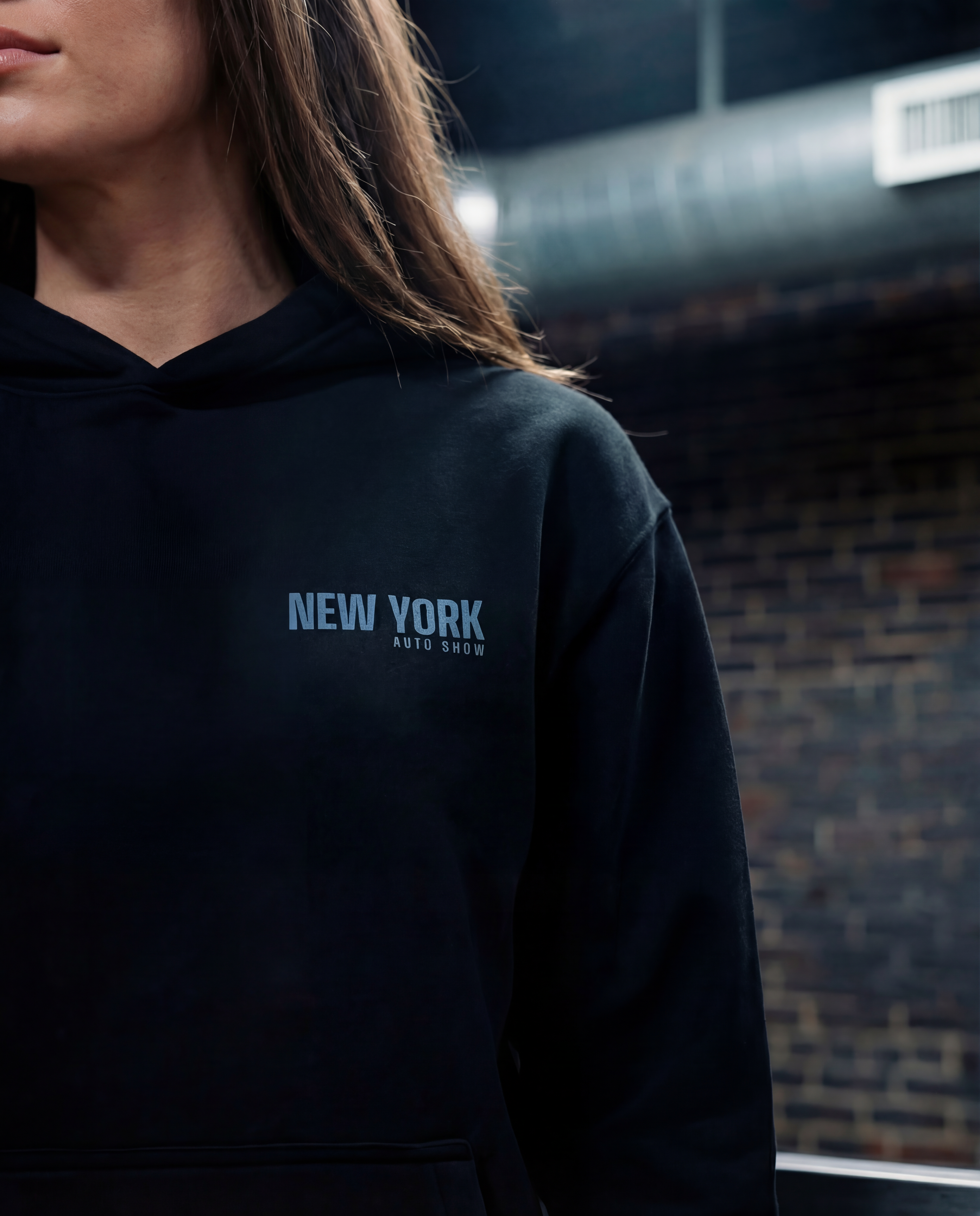 Person wearing a black hoodie with 'New York Auto Show' text against a dark background
